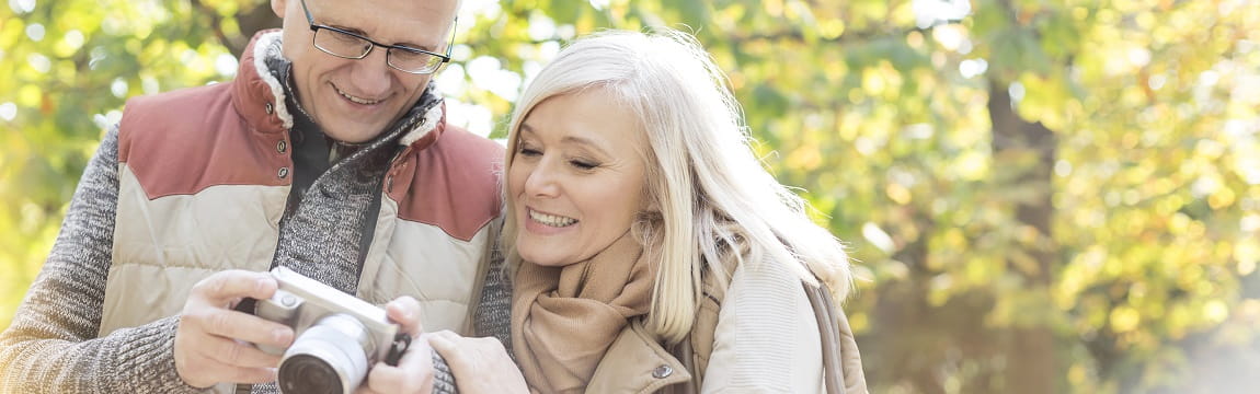 A man and woman smile and look at photos on a digital camera together. 